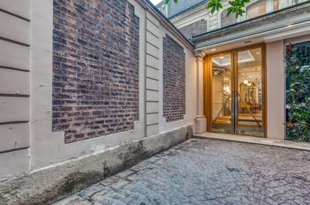 Cour pavée menant à la porte vitrée de l’atelier, où l’on aperçoit le lustre et le miroir doré