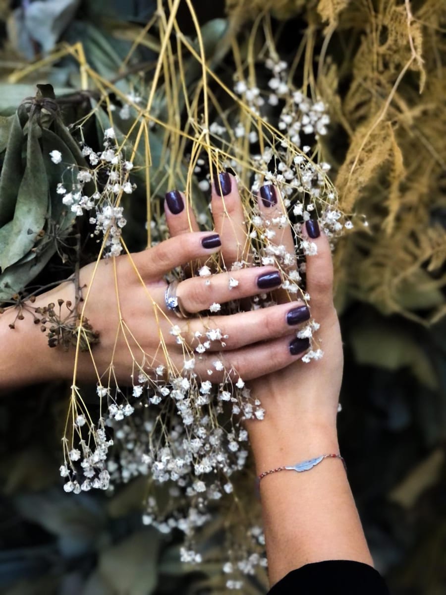 Deux mains au vernis prune parmi des fleurs séchées