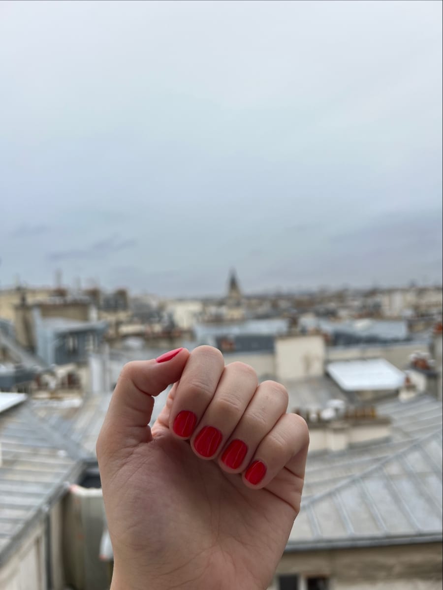 Main au vernis rouge vif devant les toits de Paris